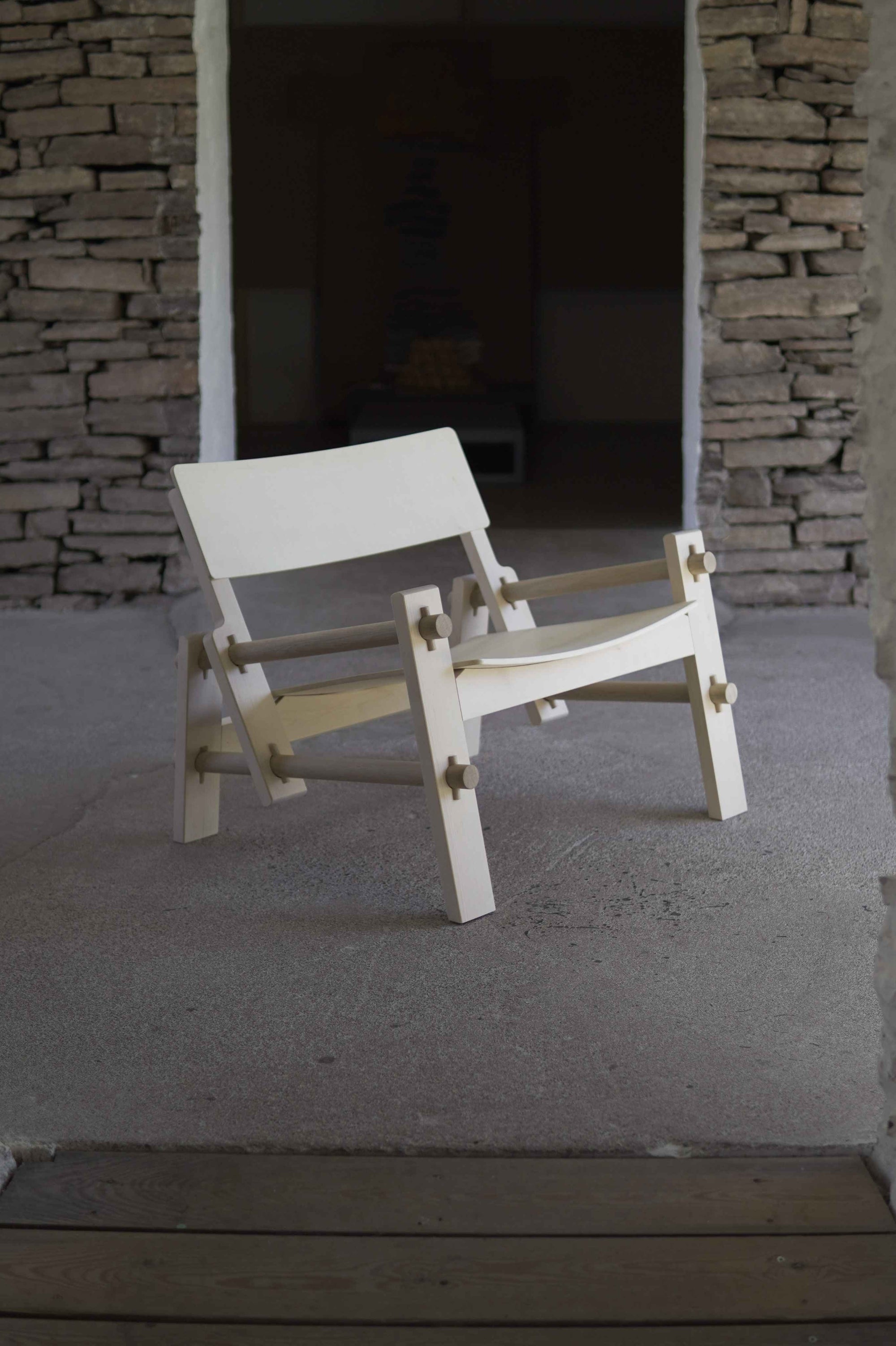 White chair with wooden frame against a stone wall.