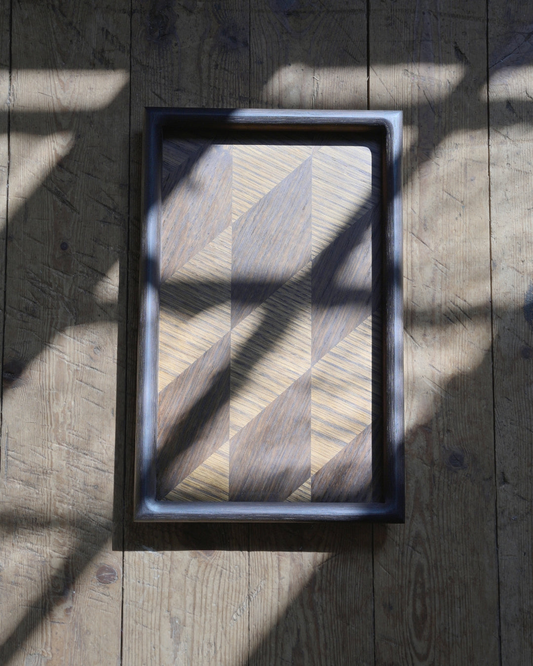 Handmade oak tray seen from above on a plank floor, its parquet pattern catching the sunlight