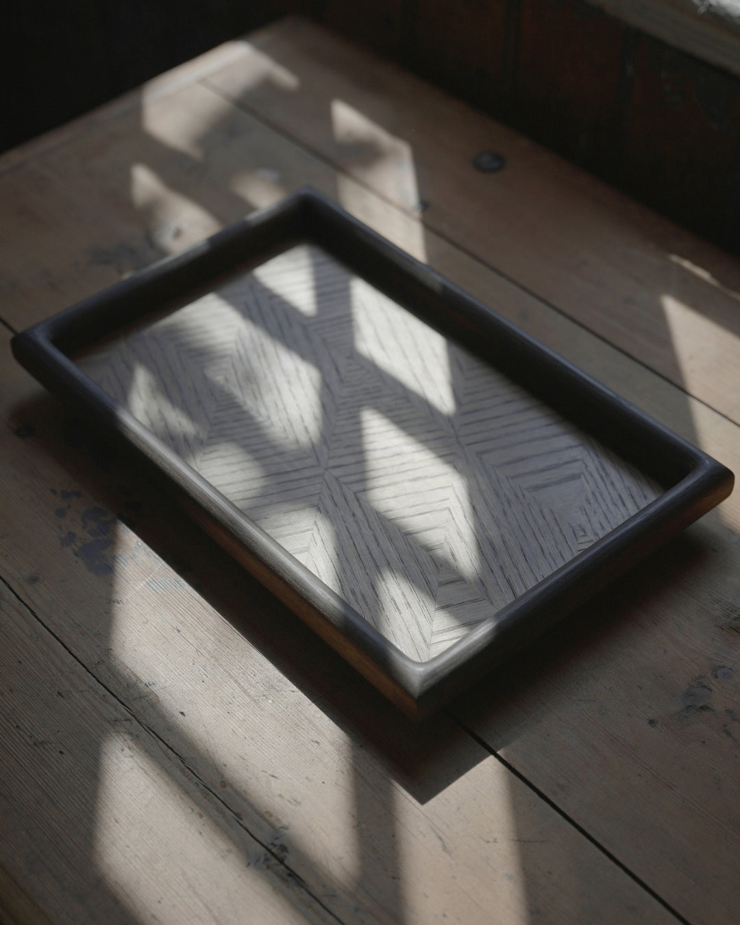 Parquet tray on a worn wooden table, with window light falling across the oak veneer pattern