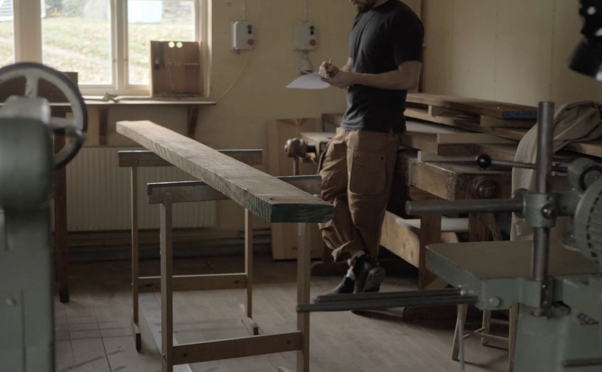 Olof Davidsson planning the coffee and tea cabinets beside a rough-sawn board in his workshop