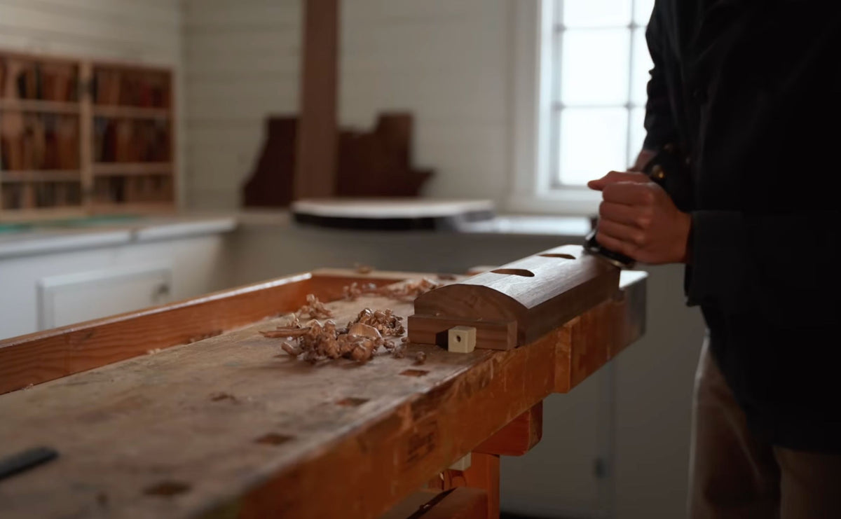 Hand-planing a walnut foot for the coffee table at a workbench covered in shavings