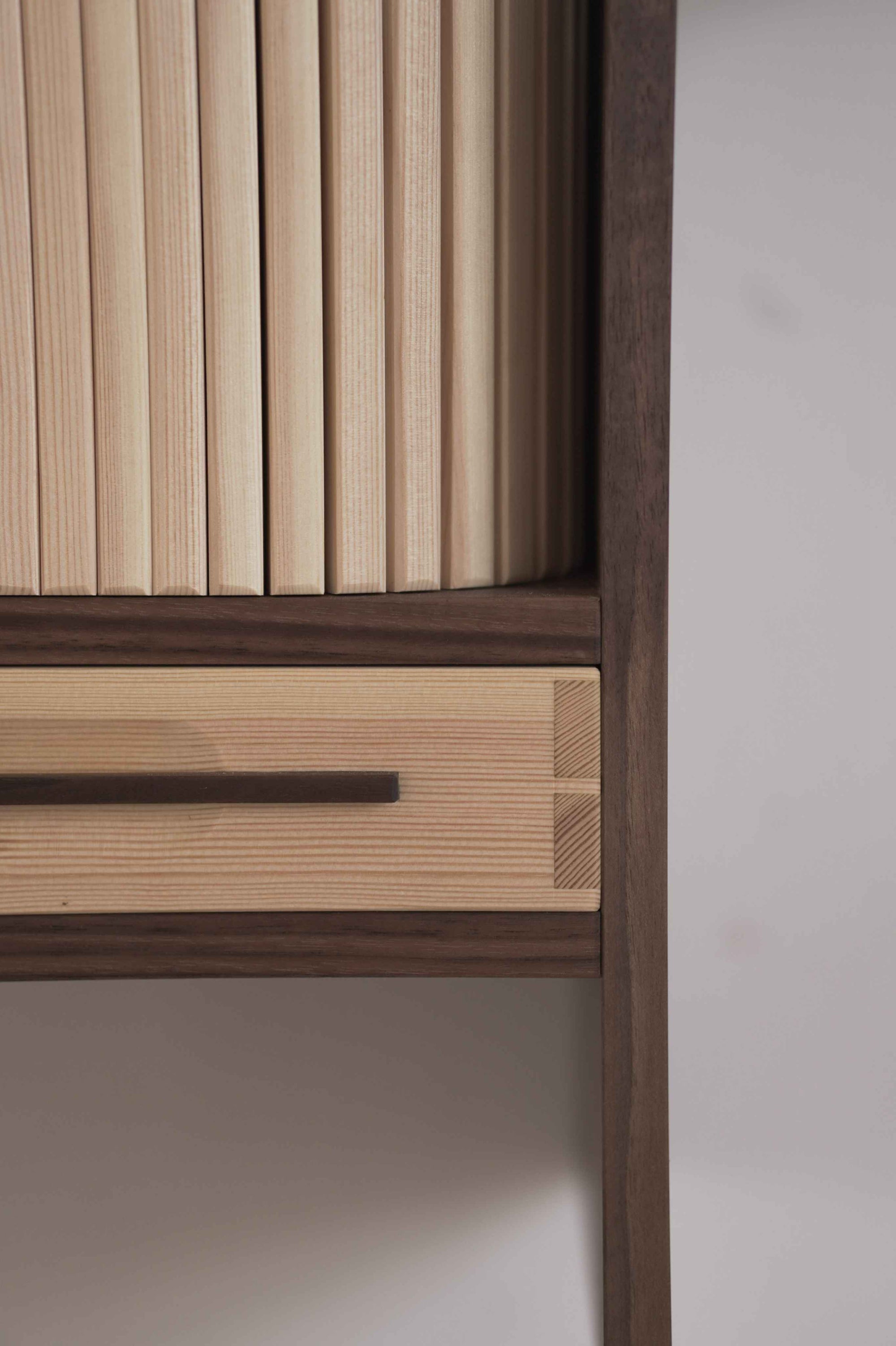 Closeup of a wooden cabinet with tambour doors on a plain wall
