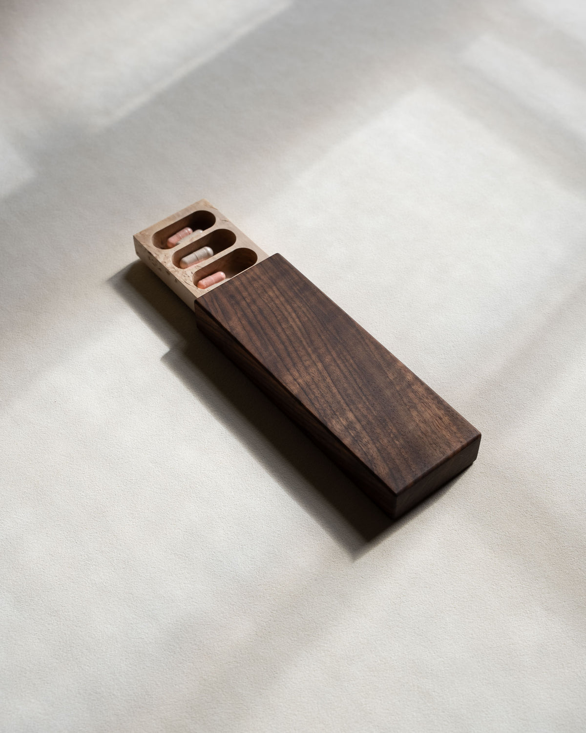 Weekly pill box in walnut and masur birch, slightly open, in soft natural light
