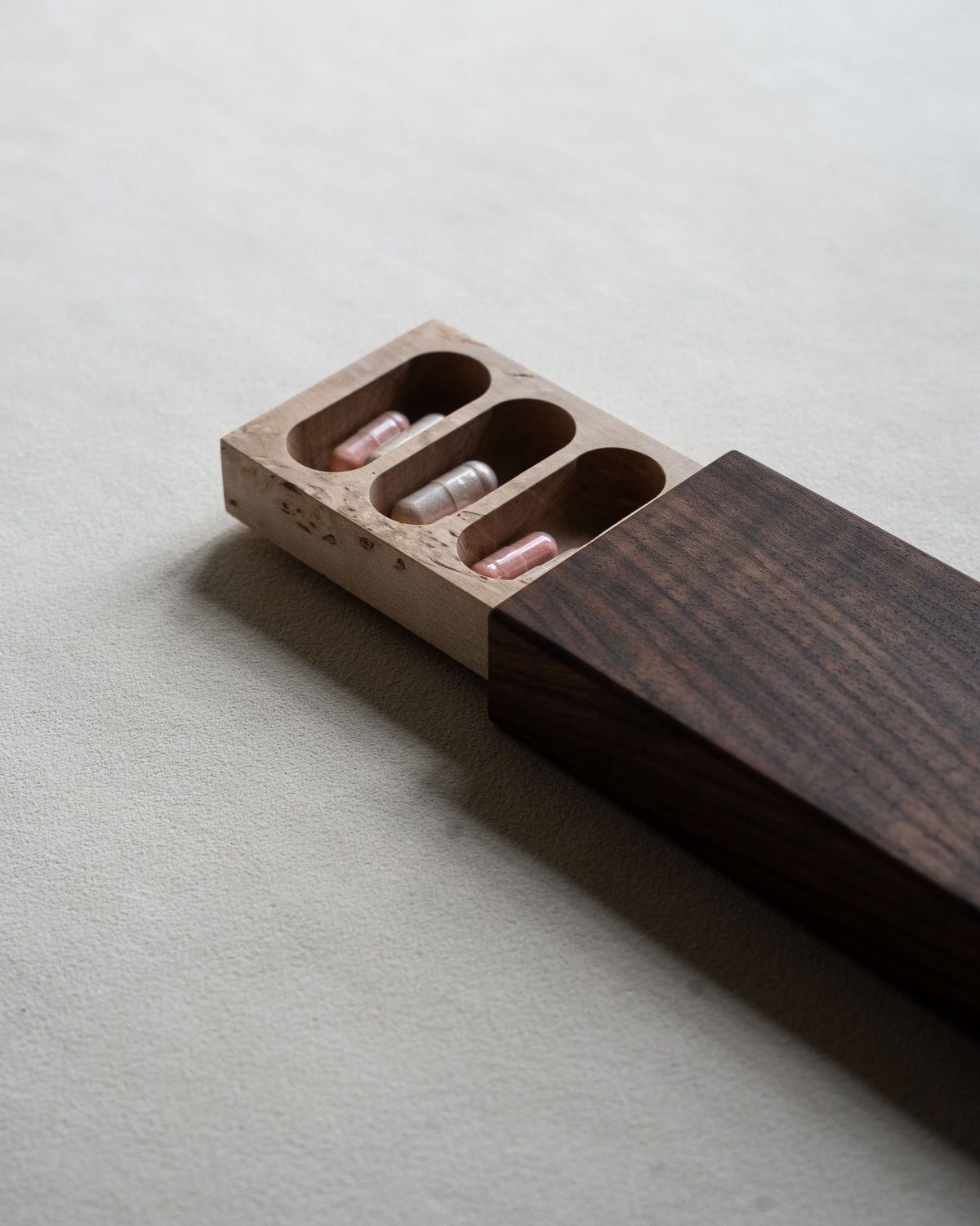 Close-up of rounded compartments carved in figured masur birch, holding capsules