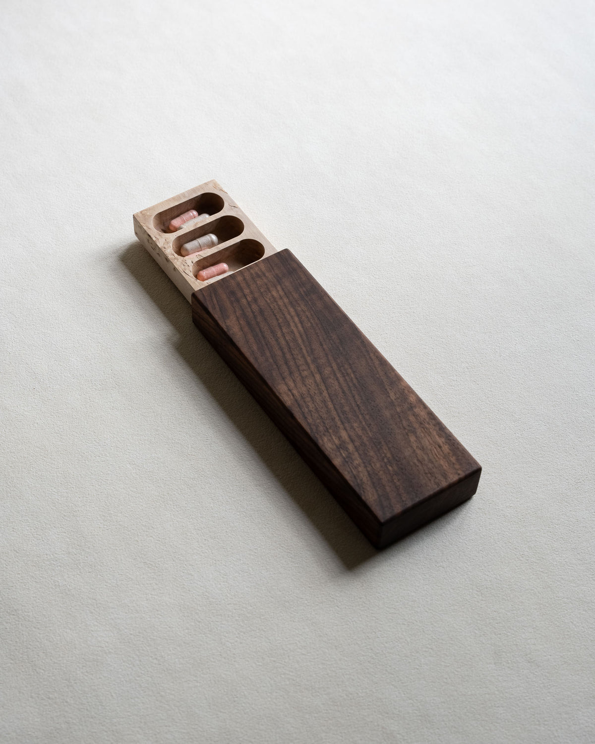 Handmade walnut pill box slid partly open to show a masur birch tray with capsules