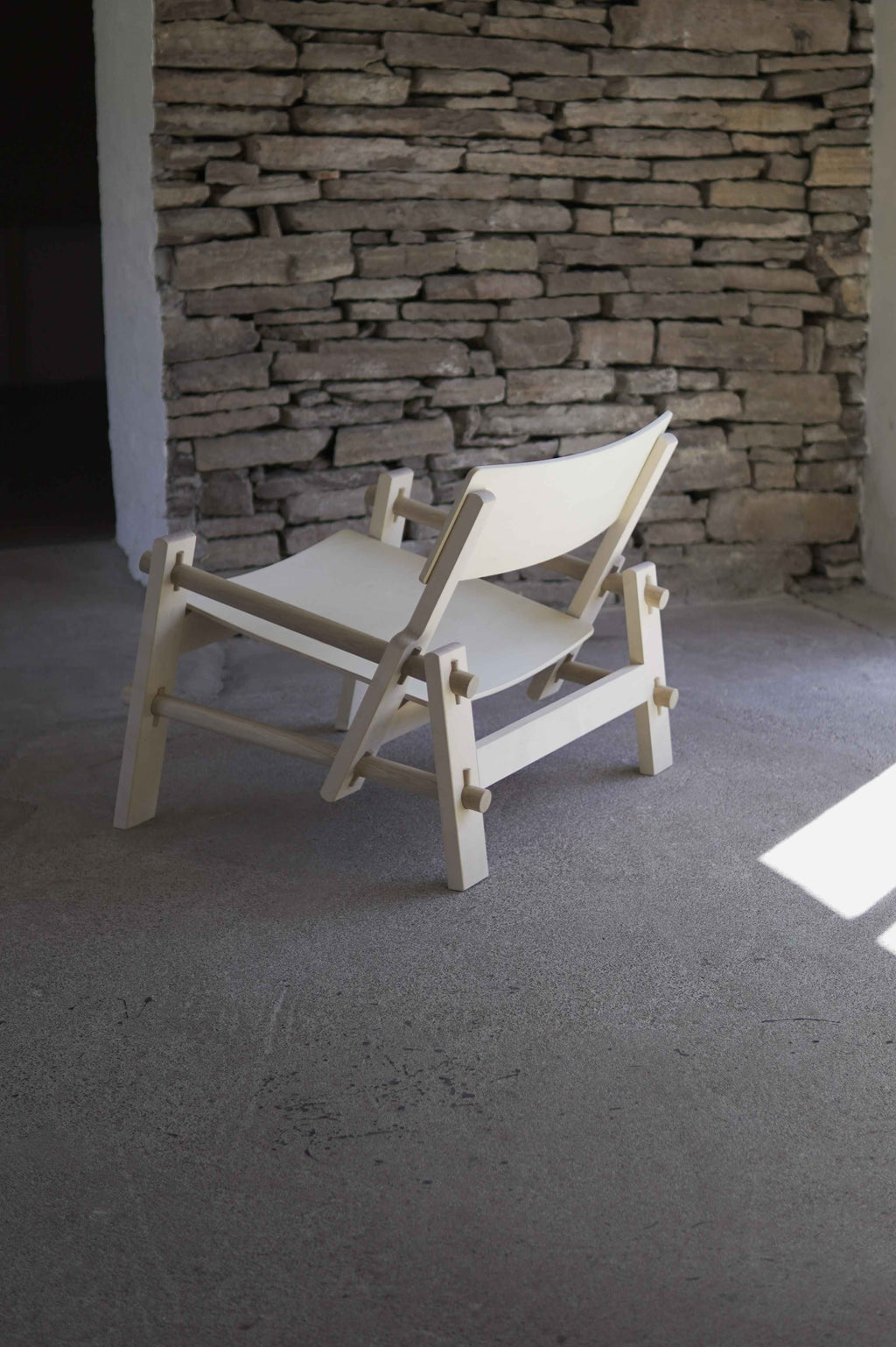 White chair against a stone wall in a room with concrete floor