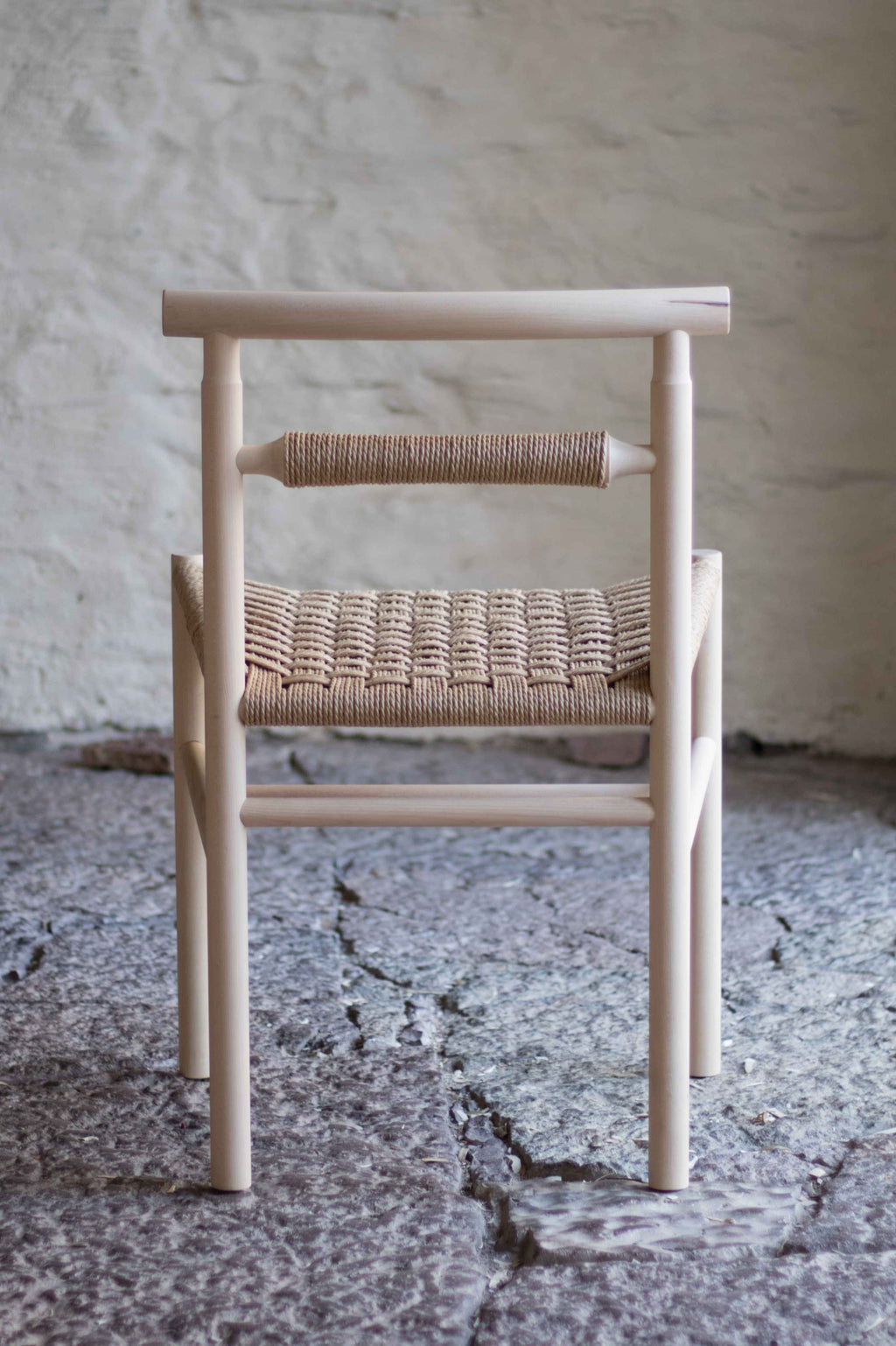 Chair with woven seat and backrest against a textured wall.