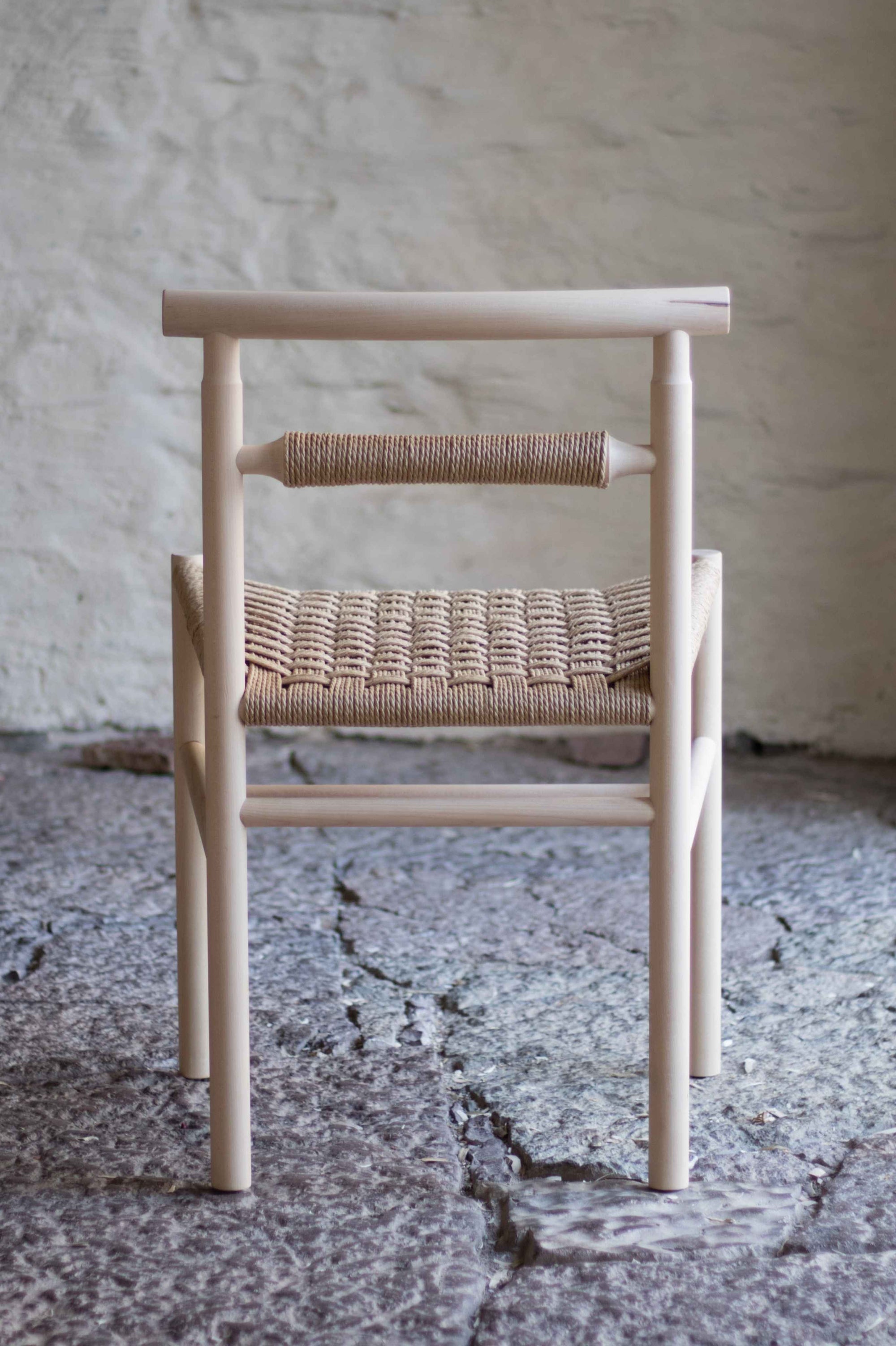 Chair with woven seat and backrest against a textured wall.