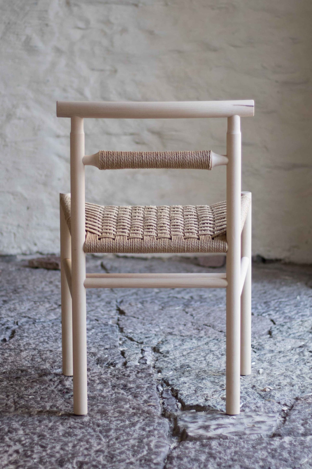 Chair with woven seat and backrest against a textured wall.