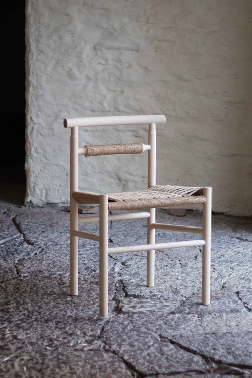 Wooden chair with woven seat on a stone floor against a textured wall.