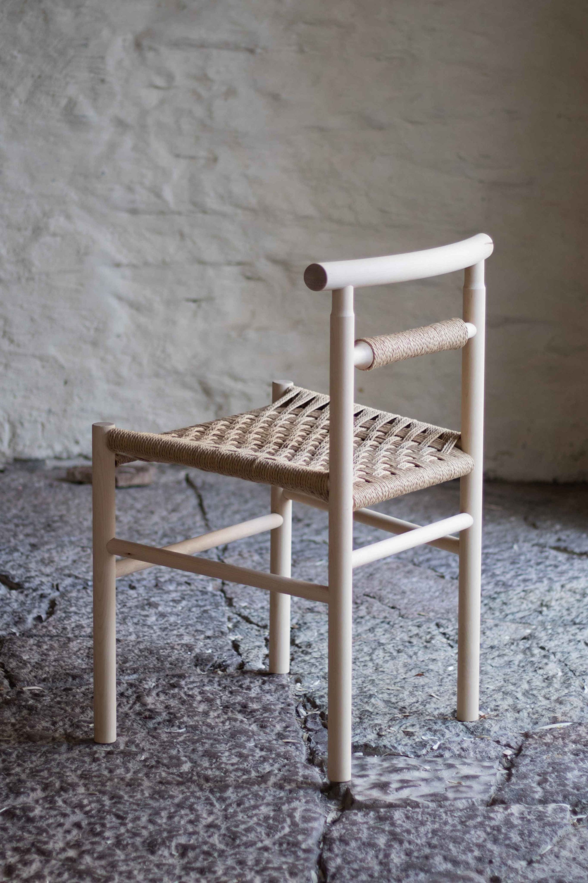 Woven chair with wooden frame against a textured wall.
