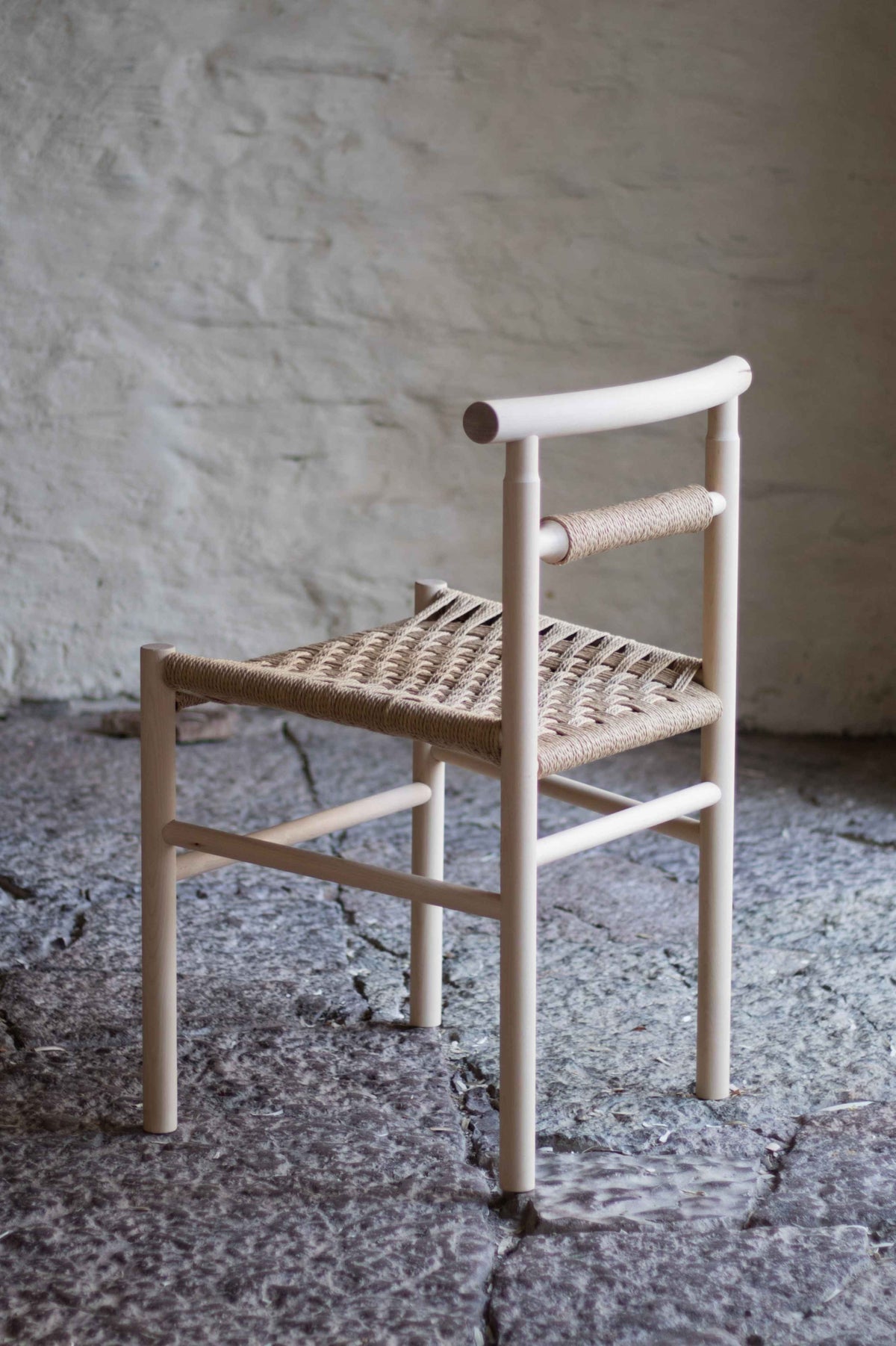 Woven chair with wooden frame against a textured wall.