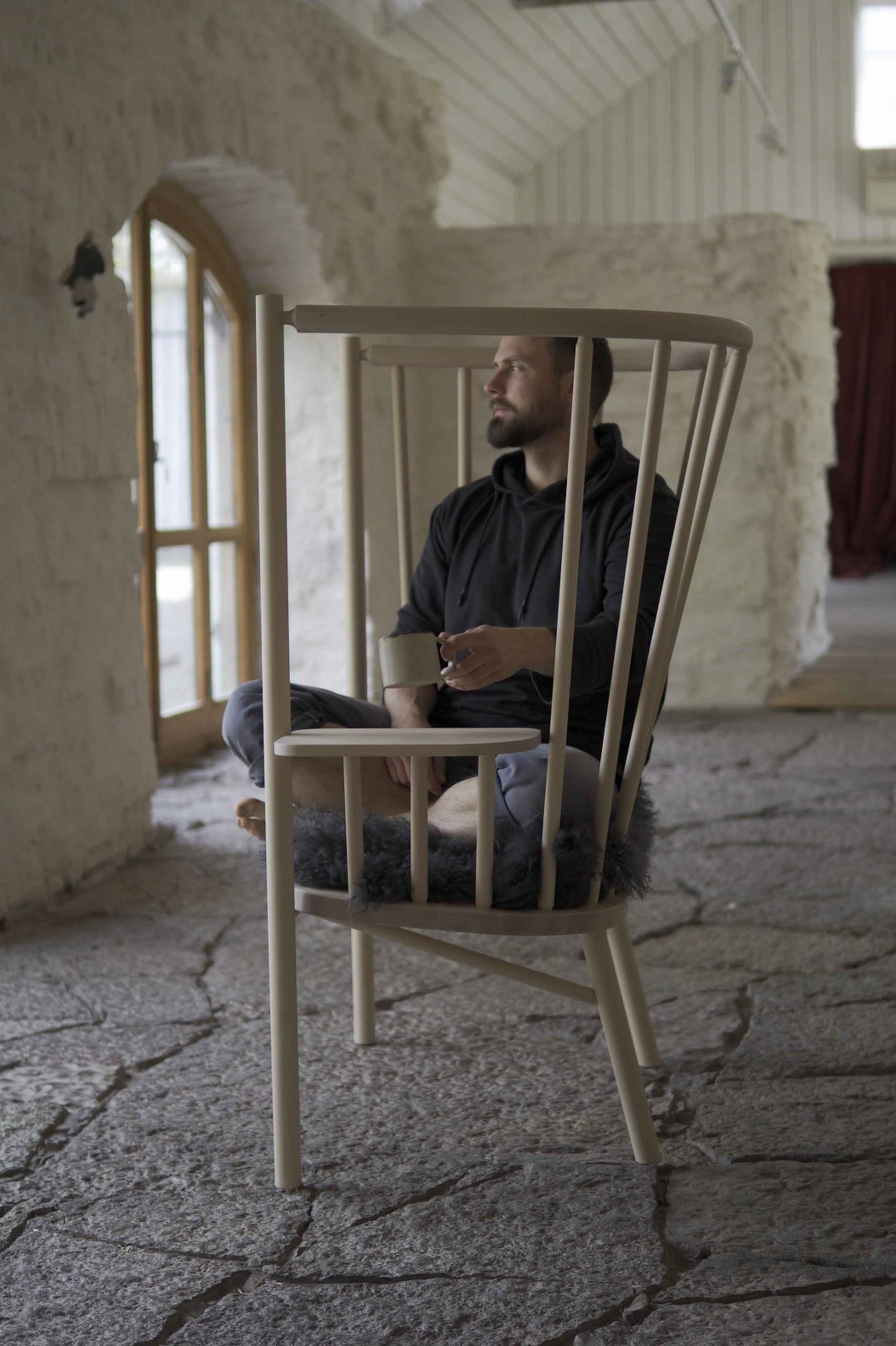 Olof Davidsson sitting inside the Spread chair, a wooden chair structure in a room with textured walls and floor.