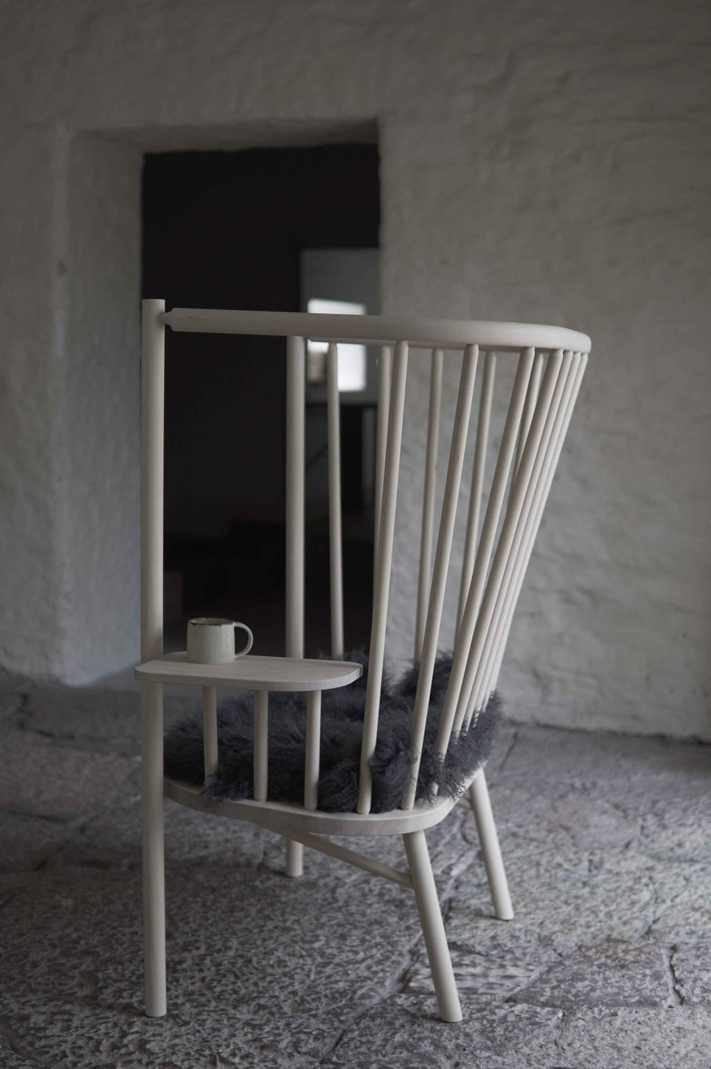 Wooden chair with a small table and cup against a textured wall.