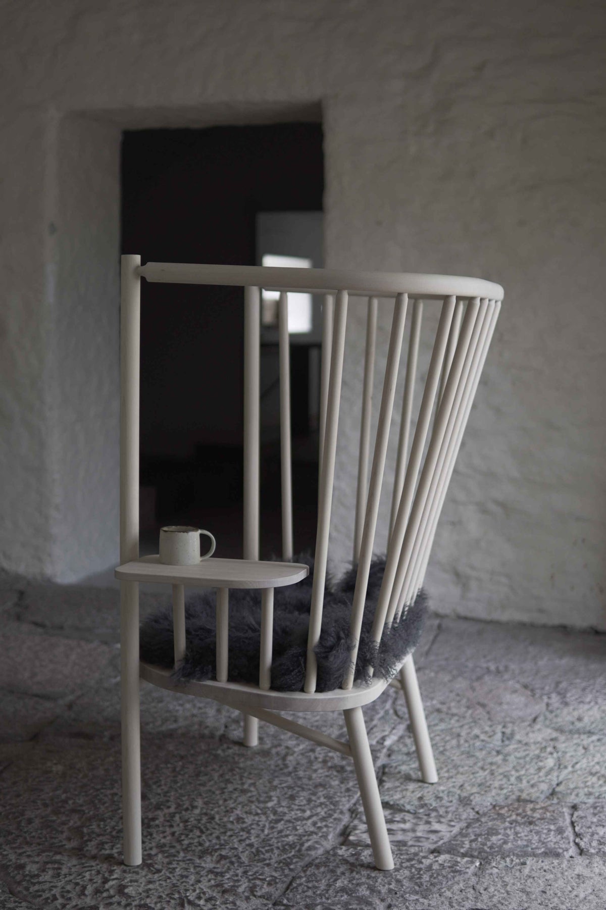 Wooden chair with a small table and cup against a textured wall.
