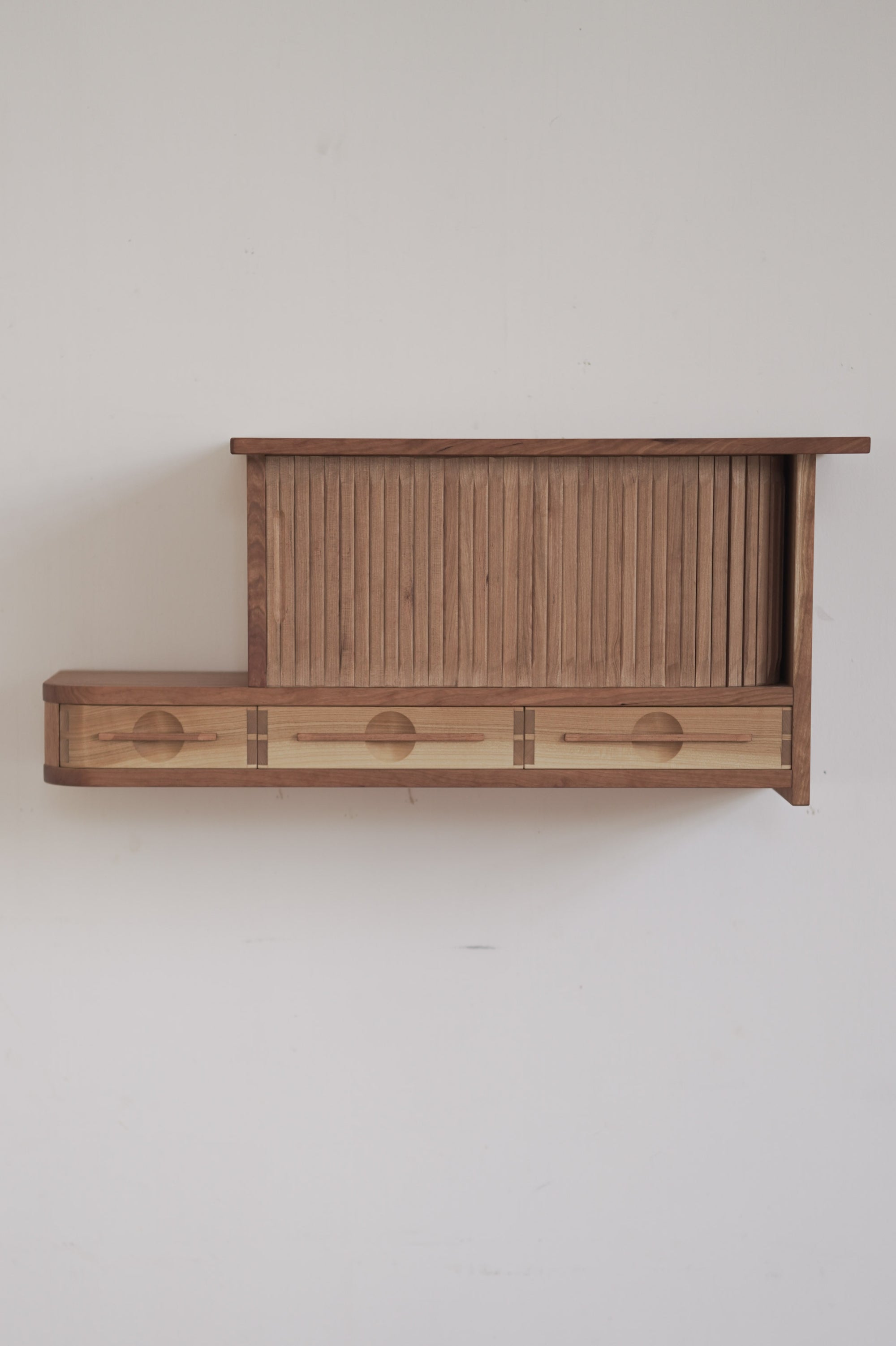 Wooden cabinet with tambour doors on a plain wall